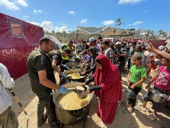 A group of people standing around large pots of food

AI-generated content may be incorrect.